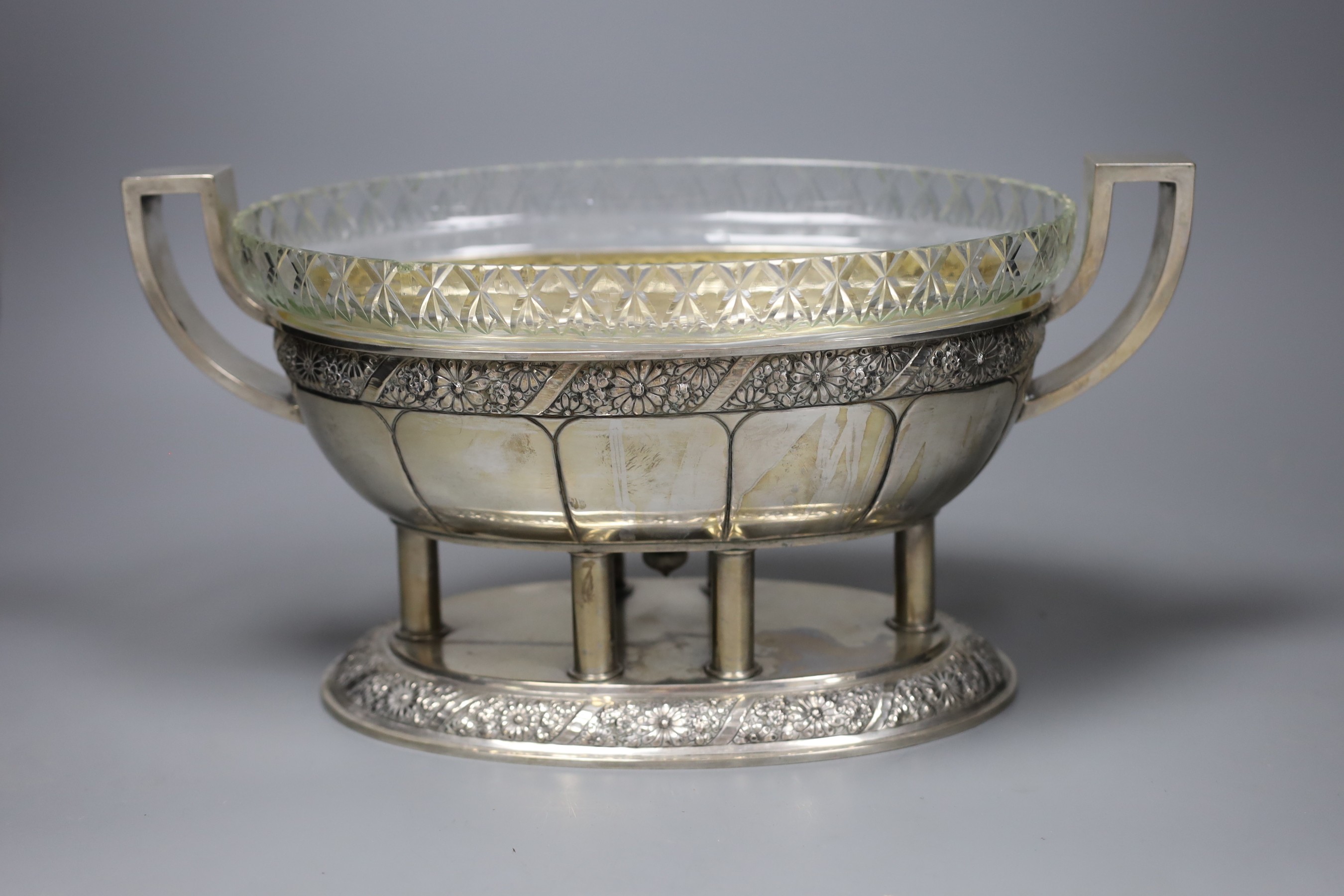 An early 20th century Continental white metal two handled centrepiece bowl, with engraved floral banded decoration and cut glass liner, 35cm over the handles.